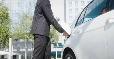 Zakenman laad elektrische auto op op zijn werk